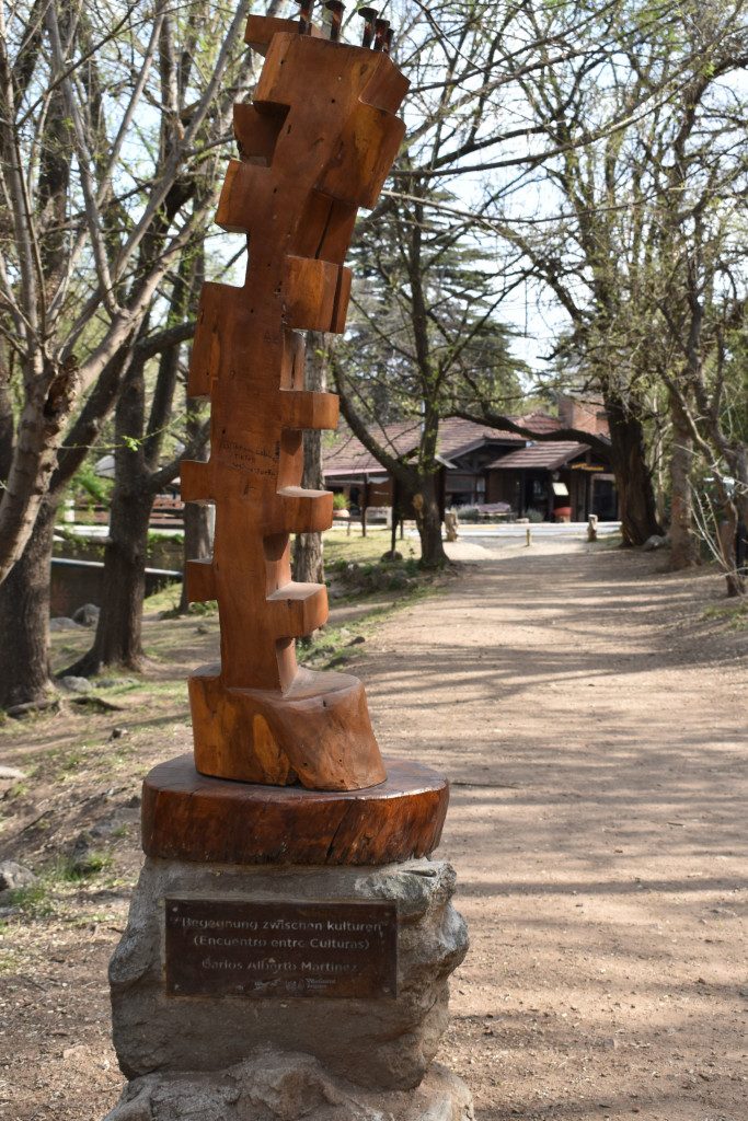 Holzfigur auf Sockel am Wegrand des Flusses