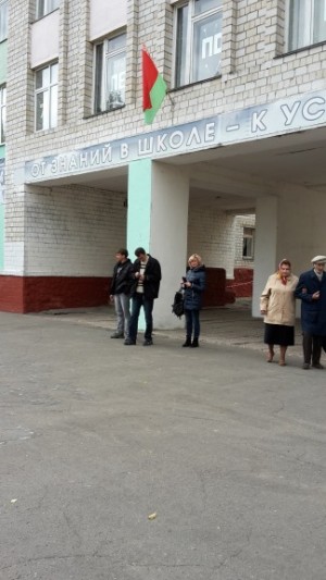 Die Fahne hängt aus und einige Menschen stehen vor der Schule.