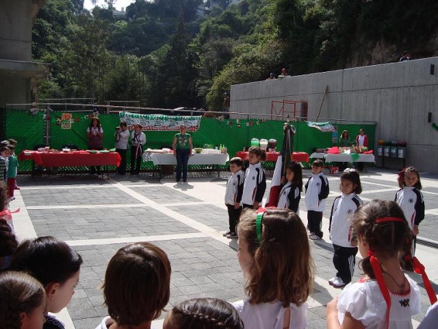 "mexikanische Kinder während der Nationalhymne, im Hintergrund das Buffet mit quesadillas, tostadas, flautas, Zimtschnecken, total süßem Esskrams und Zuckerwasser in verschiedenen Farben und Geschmacksrichtungen (Horchata, Jamaica und noch was...)"